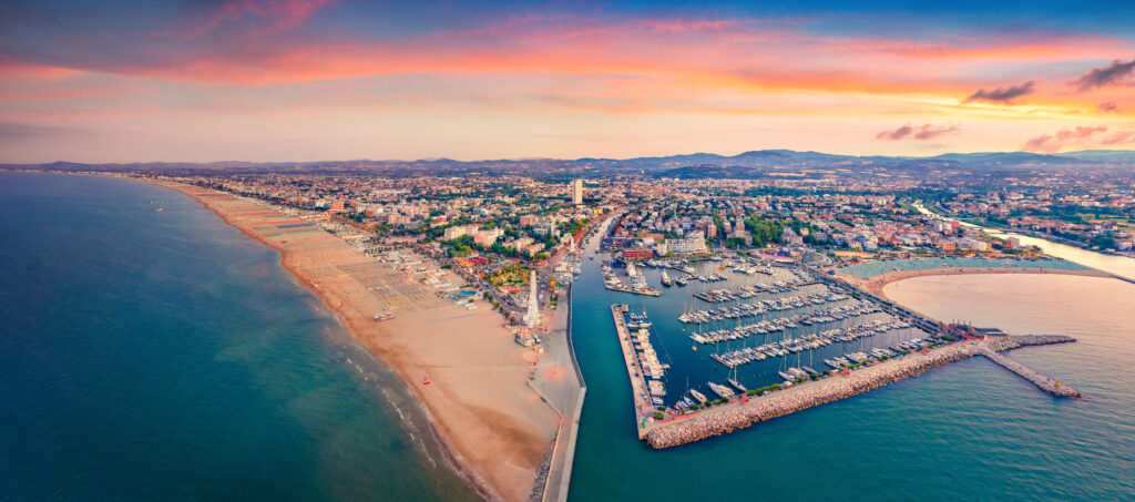 Panoramic summer view from flying drone of Libera Rimini public beach. Captivating evening scene of Italy, Europe. Colorful sunset on Adriatic coast. Vacation concept background.